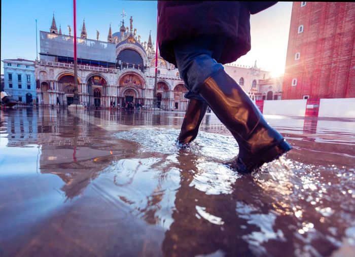 A woman wearing rubber boots strolling across St Mark's Square in Venice