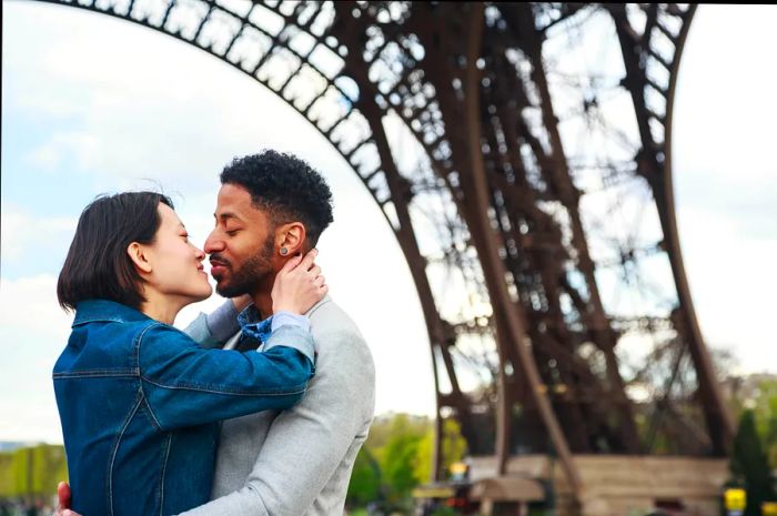 A couple shares a kiss beneath the Eiffel Tower in Paris, France