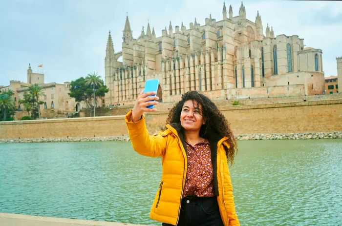 A woman captures a selfie in front of the Palma de Mallorca cathedral, located in the Balearic Islands of Spain.