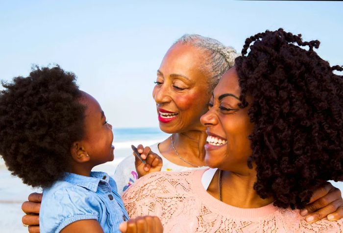 A joyful three-generation family with Afro-styled hair shares smiles and affectionate glances, relishing their time together.