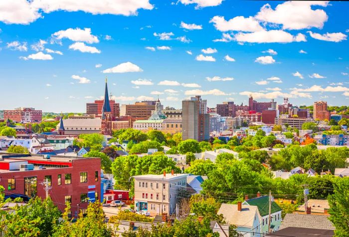 The city skyline features tall buildings, steeples, and gable-roofed homes, all set against a stunning sky.