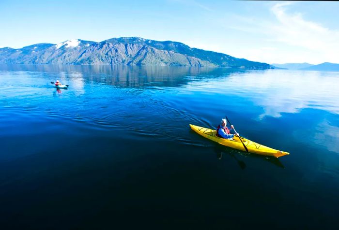 A couple enjoying a sunny day on a lake, each in a yellow Dinogo, with a stunning mountain backdrop.