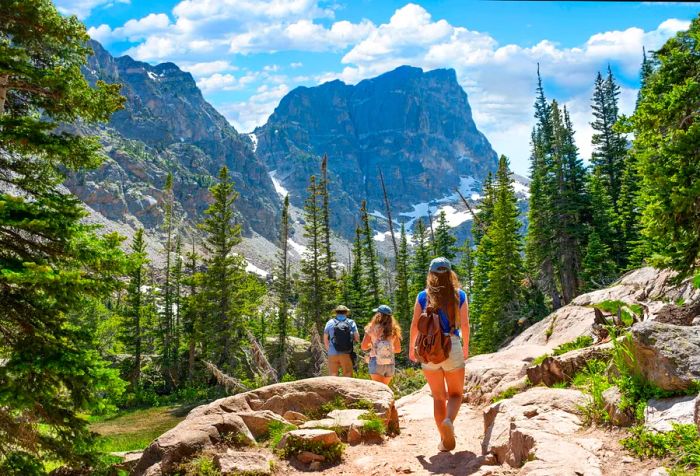 A father guides his two daughters on a hiking adventure in the mountains.