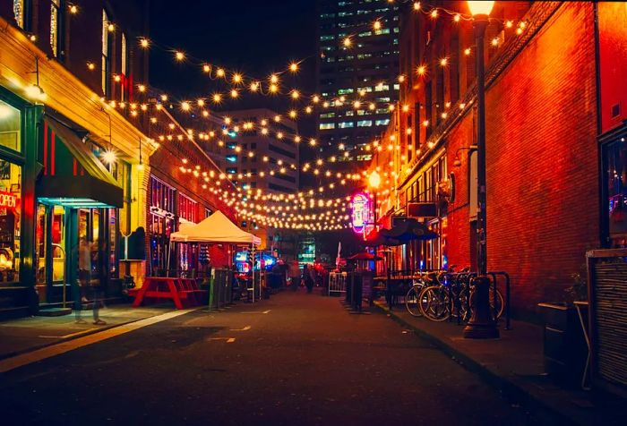 Twinkling string lights illuminate a street filled with pubs and restaurants.