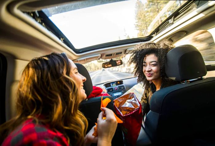 Two friends enjoying a chat in a car while munching on chips.