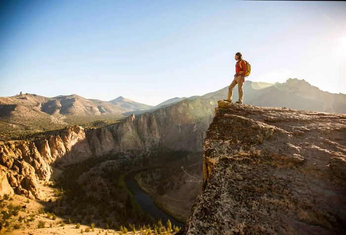 A hiker stands at the cliff's edge, gazing down at the river winding through the steep canyons.