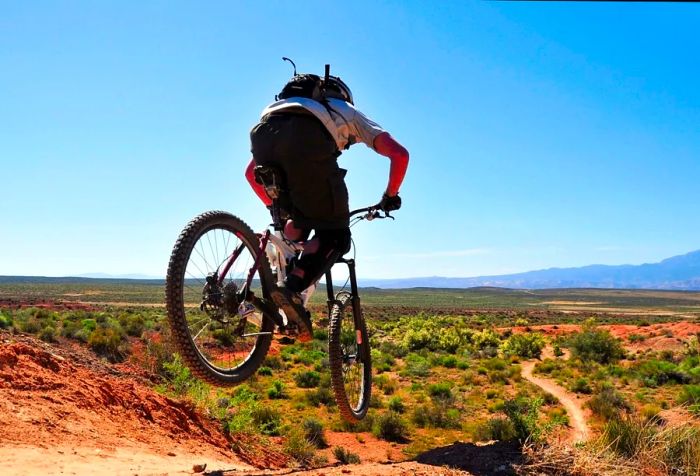 A man confidently rides his bike across a vast, open grassy expanse, soaking in the beauty of the clear blue sky overhead.