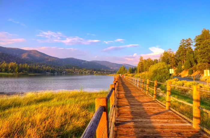 The rustic wooden boardwalks of Stanfield Marsh line the stunning shores of Big Bear Lake, framed by a brilliant blue sky and lush mountain forests.