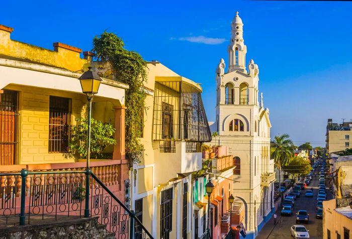 A white church towers over a bustling city street filled with parked vehicles.