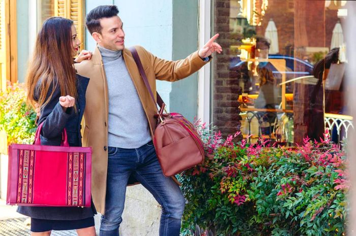 A stylish heterosexual couple stands near a shop window, pointing while enjoying a day of shopping in the city