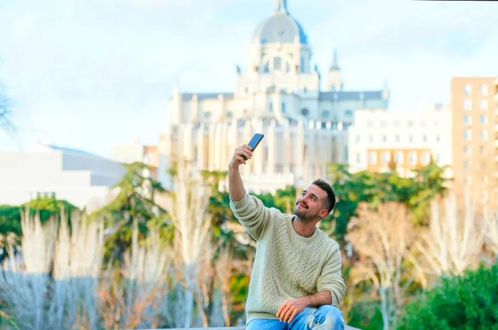 A man capturing a selfie with the Almudena Cathedral in the background, Madrid, Spain.