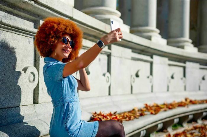 A woman with an afro takes a selfie in front of a monument at Retiro Park in Madrid