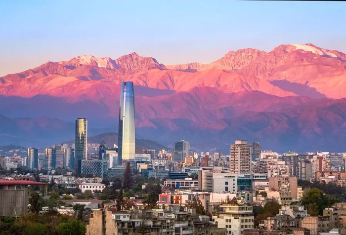 The Gran Torre Santiago, a striking 62-storey skyscraper, stands out against the backdrop of sunlit mountains.