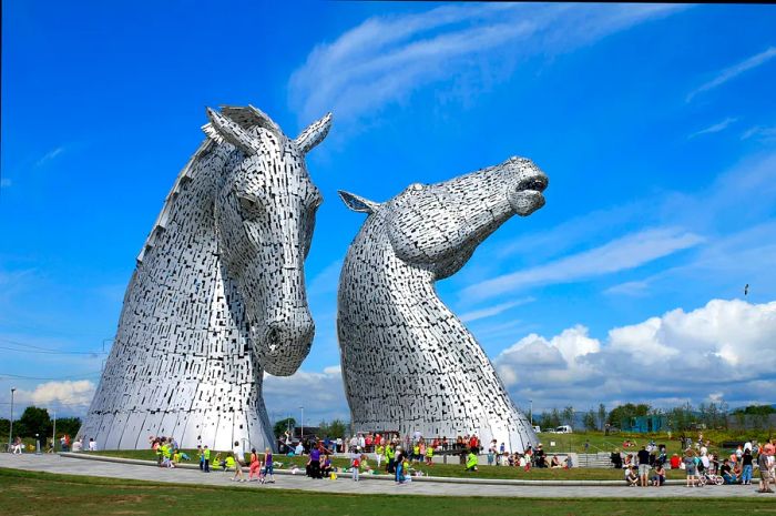 Two enormous horse-head sculptures located by a canal, attracting visitors.