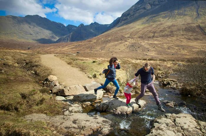 A family with a small toddler walks along a hiking trail, crossing a stream along the way.