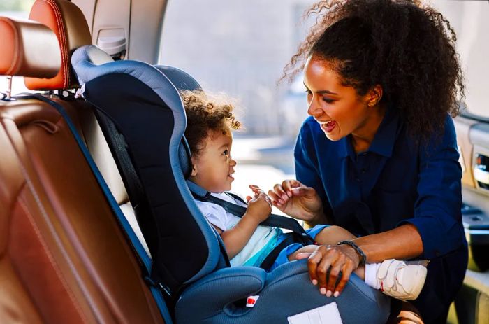 Joyful mother gazing at her child in a car seat. Young woman getting her kid ready for a journey. THEME_PERSON_PARENT_CHILD_CAR_CAR-SEAT-GettyImages-1189927309