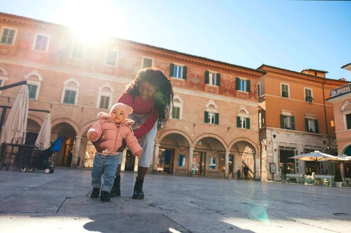 A mother strolls with her baby girl in an Italian city square.