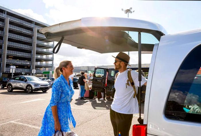 Two people animatedly discussing in the back of a white van parked in a large parking area.