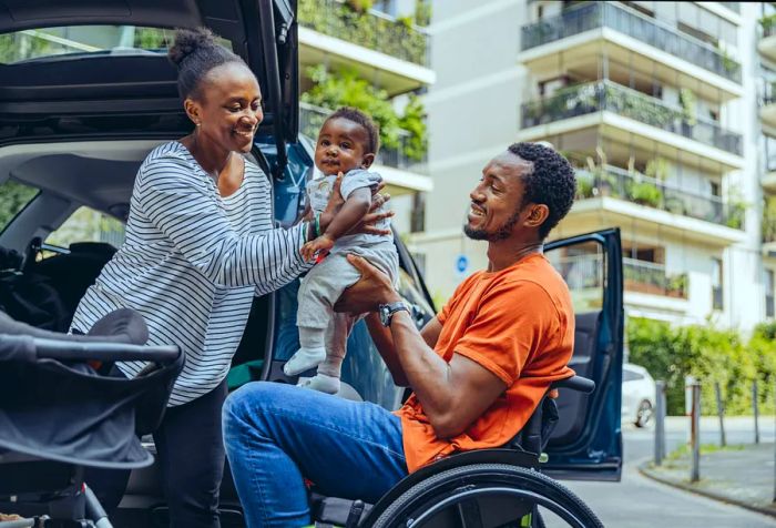 A man in a wheelchair handing a baby to a woman.