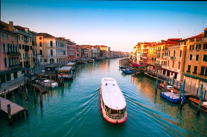 A vaporetto glides along the Grand Canal in Venice, Italy, viewed from the Rialto bridge at sunrise.