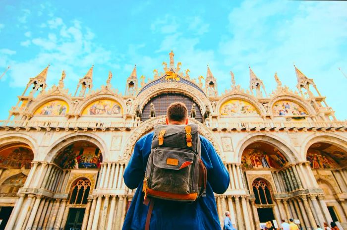 A tourist with a backpack in front of the Basilica di San Marco in Venice, Italy. Perfect for summer travel.