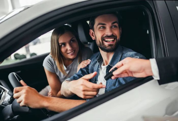 Two cheerful people gaze out the driver's window of a car.