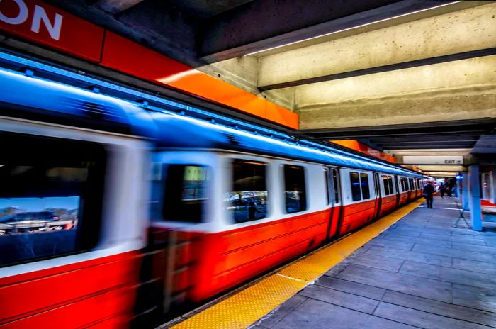 An orange train speeds through Wellington MBTA Station in Boston, Massachusetts