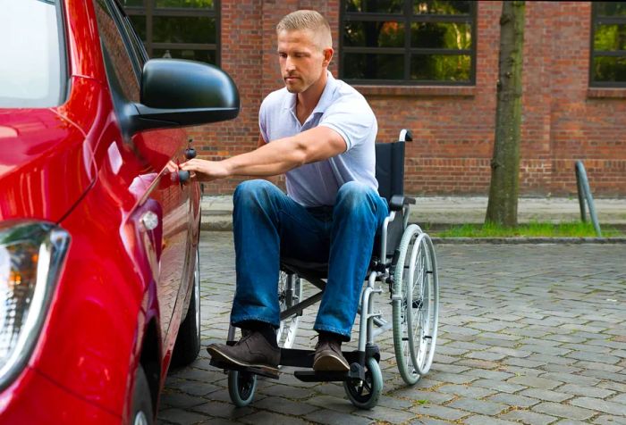 A man in a wheelchair is opening the door of a red vehicle.