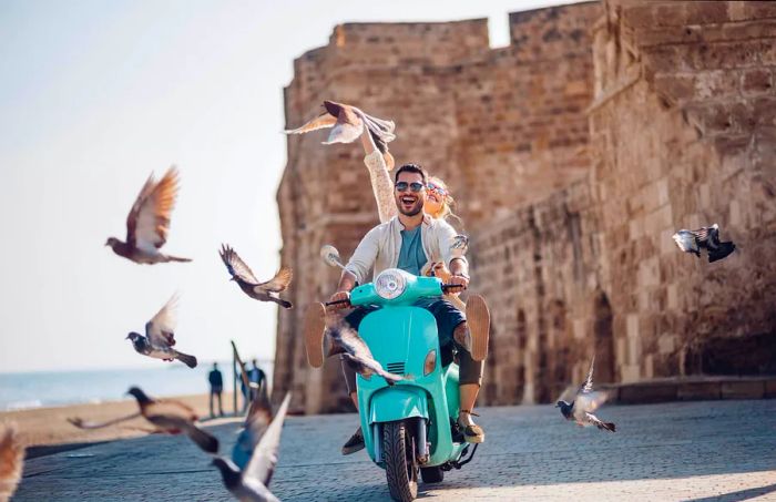 Friends enjoying summer vacations in Europe having fun riding a vintage scooter by the seaside