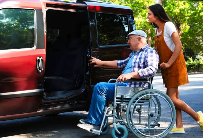 A young woman assisting an elderly man in a wheelchair as they approach the van's entrance.