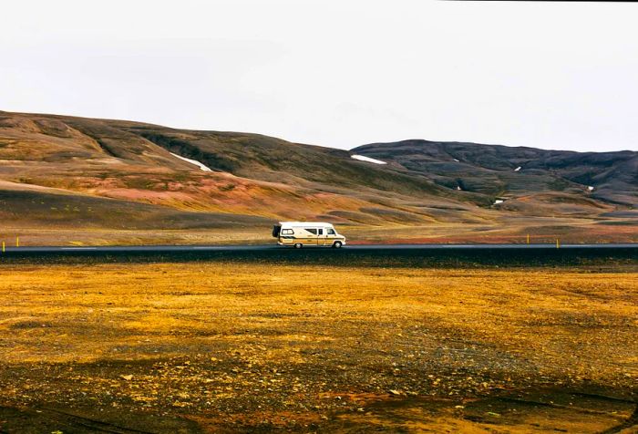 A motorhome driving along a road flanked by barren mountains and open plains.