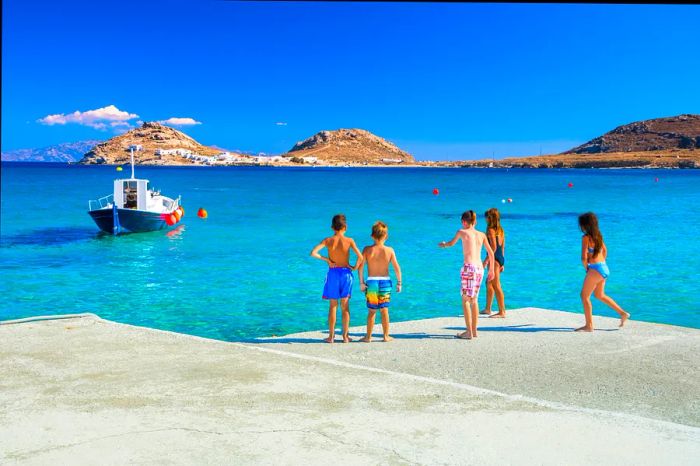 A group of children getting ready to leap into the sea from the pier at Kalafati Beach on Mykonos, Greece