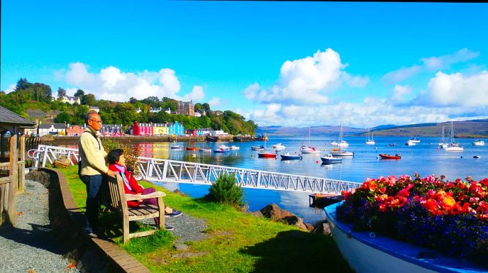 A couple relax on a bench in a picturesque harbor town adorned with colorful buildings