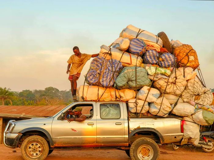 A young man perches atop a truck filled with cargo.