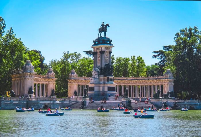 Small blue boats drift across the artificial lake, framed by the majestic equestrian monument of a king.