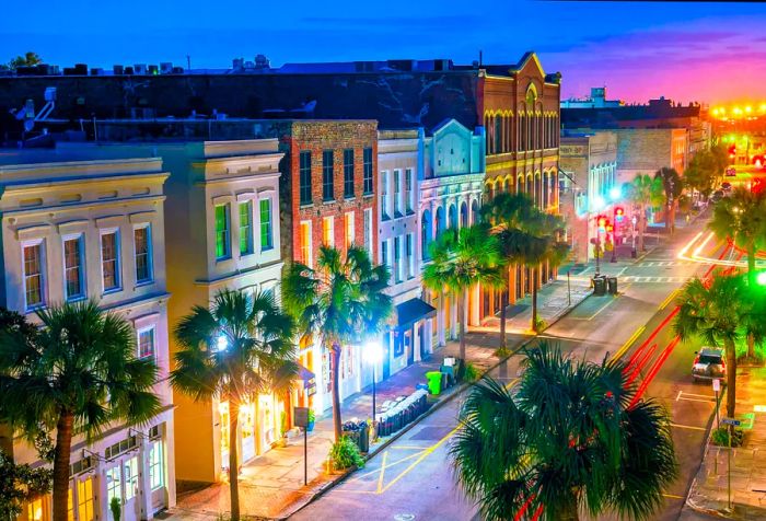 A tranquil street at night, lined with trees and glowing lampposts against the backdrop of colorful buildings.