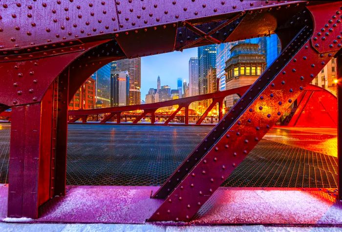 The imposing metal structure of a bridge adorned with multiple studs, overlooking a dazzling city skyline.