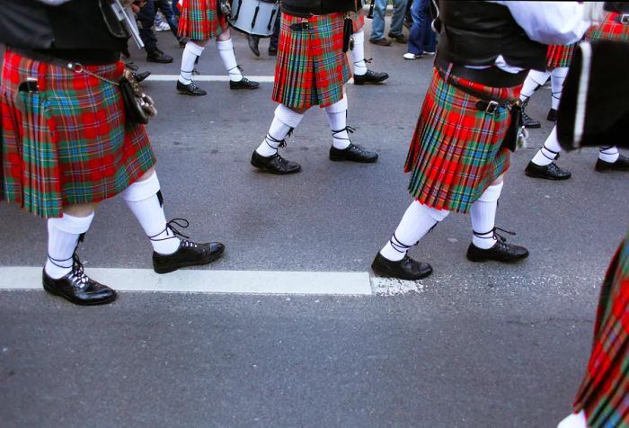 A procession of individuals parading on the street in traditional kilts.