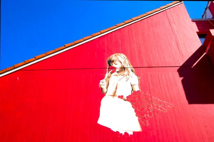 A mural in Stavanger depicting a young girl in a white dress against a vibrant red wall