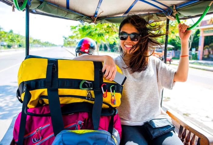 A woman wearing sunglasses beams as she relaxes in the back of a vehicle stacked with luggage.