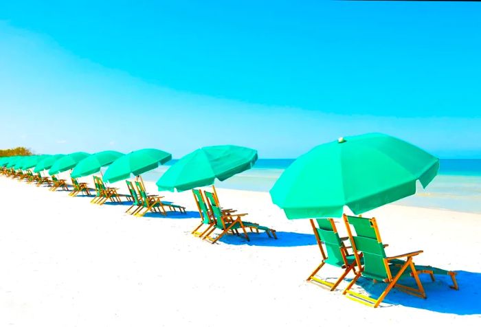 A row of sun loungers shaded by green umbrellas on a pristine white sand beach.