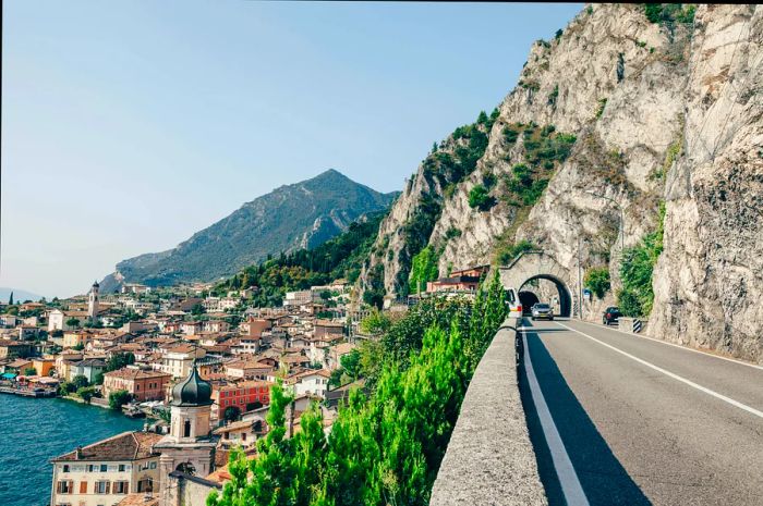 A car navigating through a tunnel on a picturesque route along Lake Garda, with the charming village of Limone sul Garda in view.