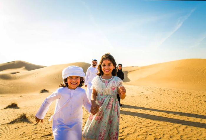 A family of four in traditional attire enjoying the desert, with the mother, father, and son in customary Muslim clothing, while the daughter wears a vibrant dress.