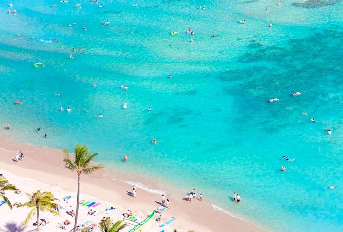 Numerous beachgoers enjoy swimming in the shallow, turquoise, crystal-clear waters.