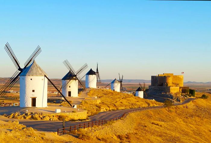 A series of windmills with white towers and pointed roofs line the roadside.