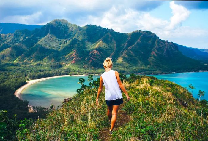 A woman strolls toward the hilltop that overlooks a beach with milky blue waters.