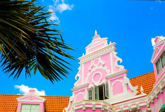 An intricately designed baby-pink window set against an orange tiled roof.