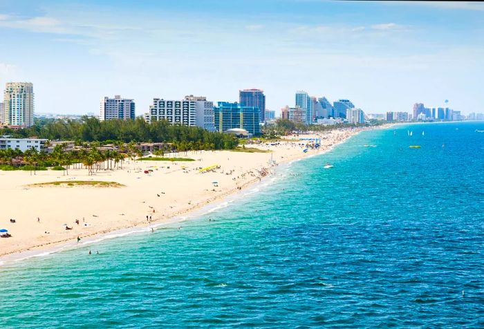 A long stretch of sandy beach flanked by tall buildings, bustling with visitors enjoying a sunny day.