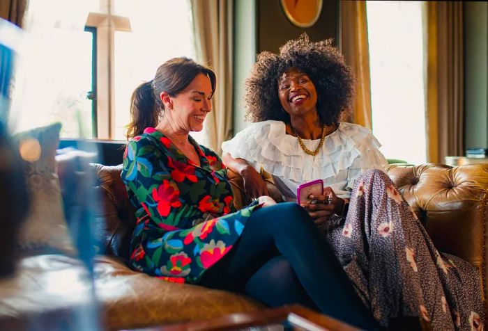 Two women are seated on a couch, sharing a laugh together.