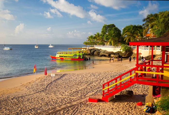 A vibrant red lifeguard tower stands watch over a beach where tourists are arriving from a boat.